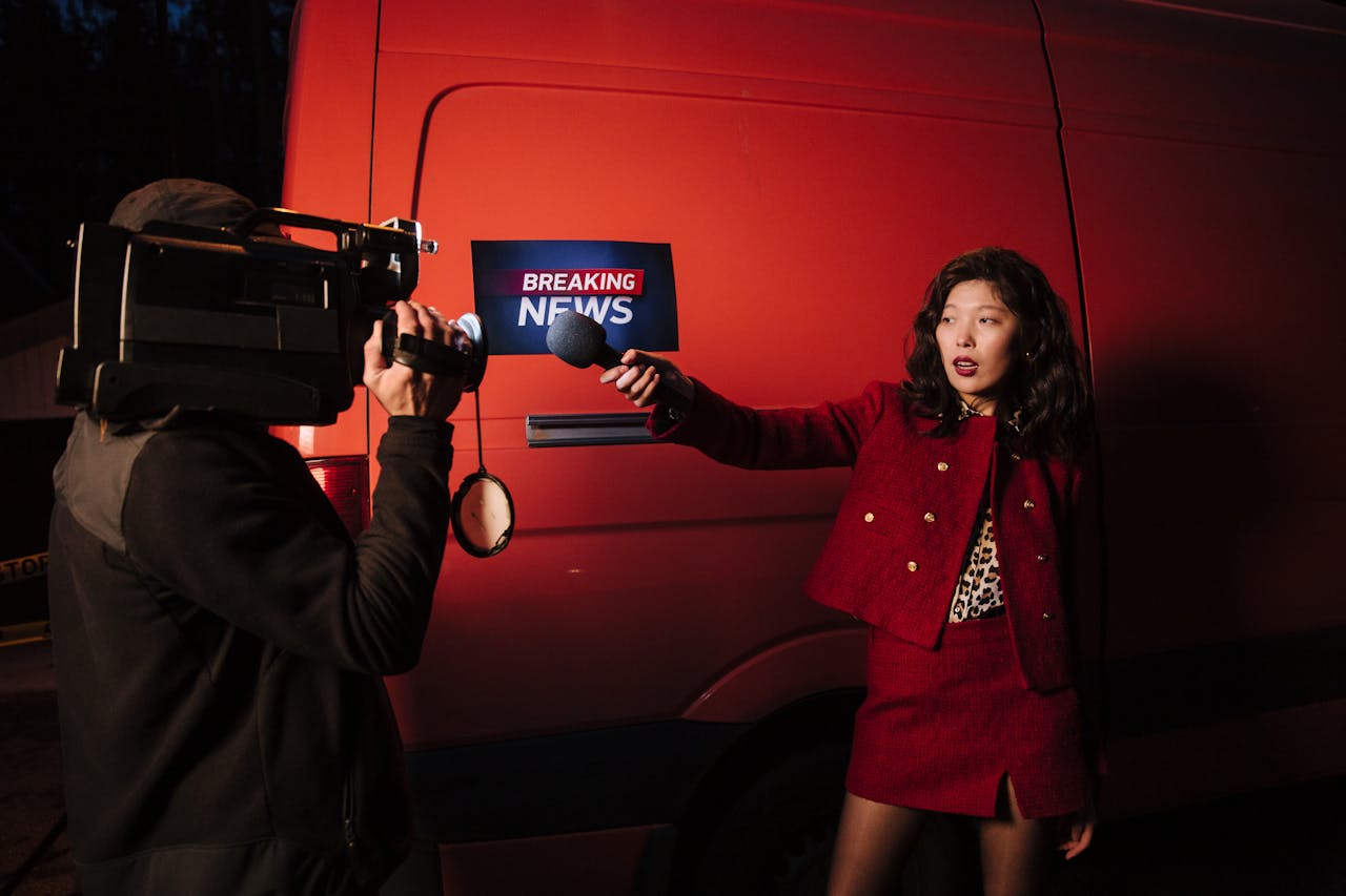 Asian female reporter with cameraman conducting a nighttime news broadcast beside a news van.