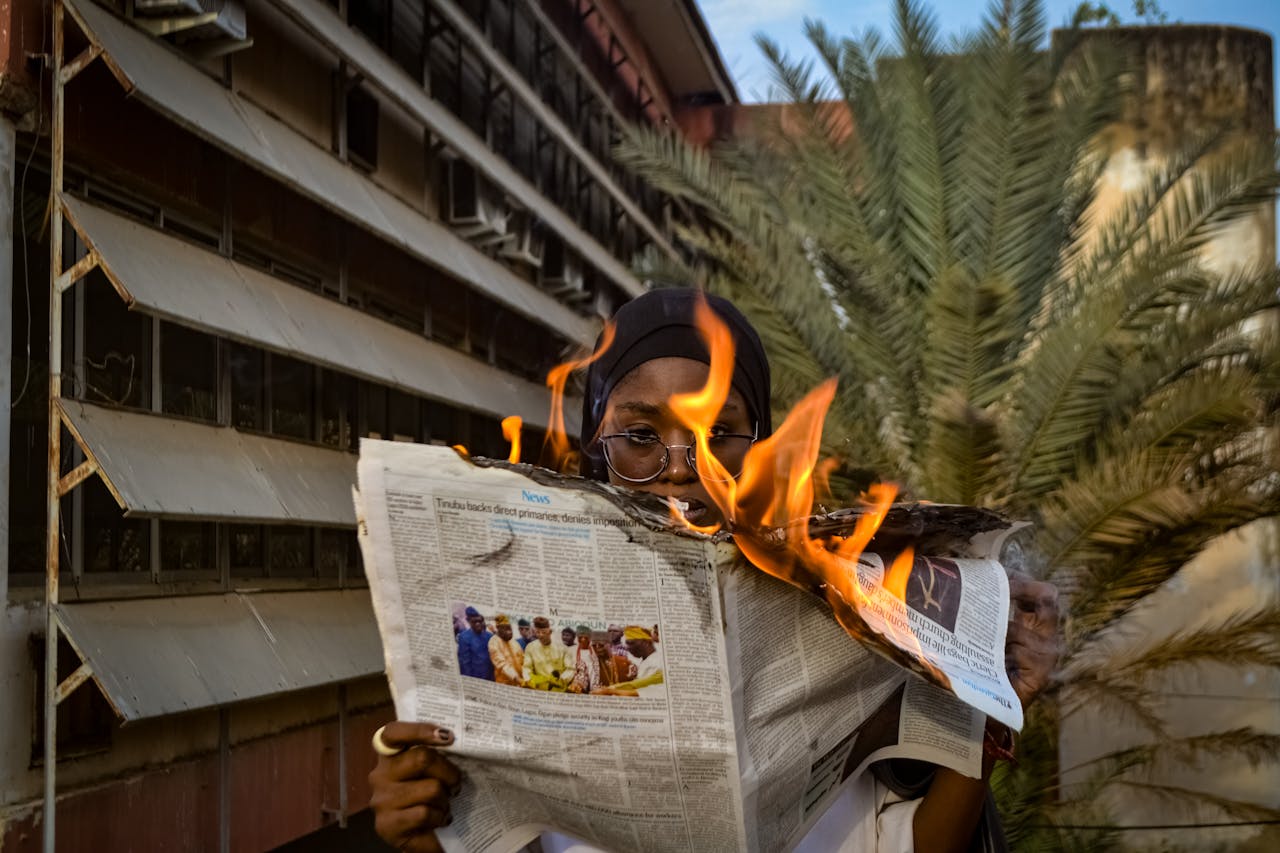 A person holds a burning newspaper outdoors, creating a dramatic and impactful scene.