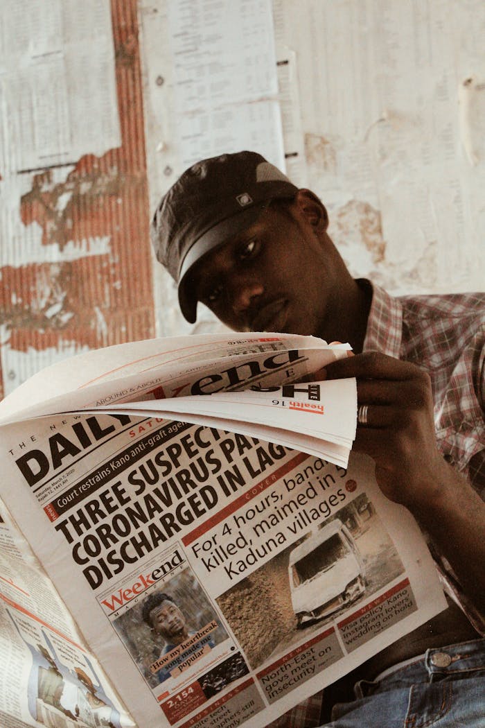 Casually dressed man reading a newspaper indoors, focusing on headlines.
